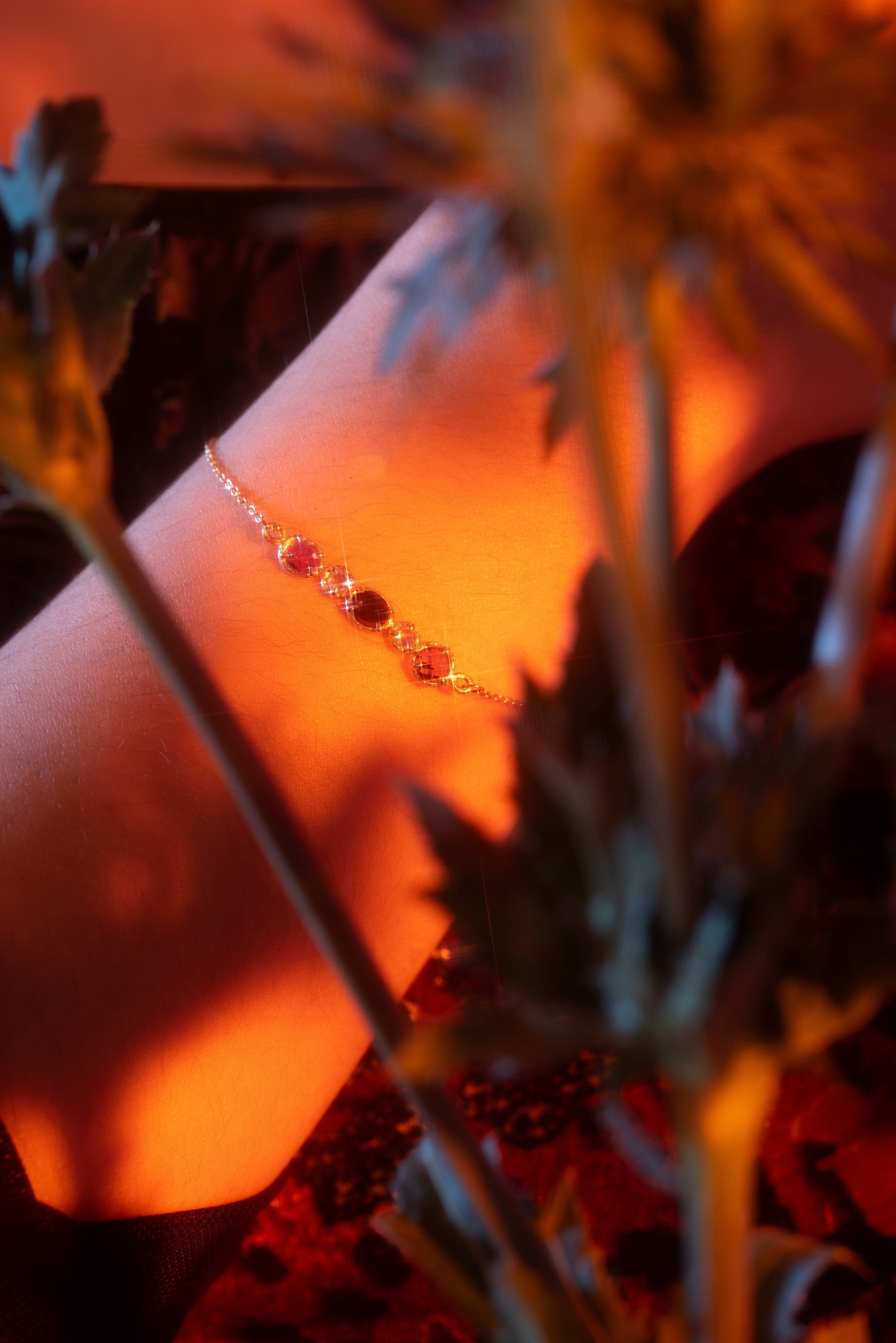 Close-up of a wrist with a bracelet surrounded by plants in warm lighting
