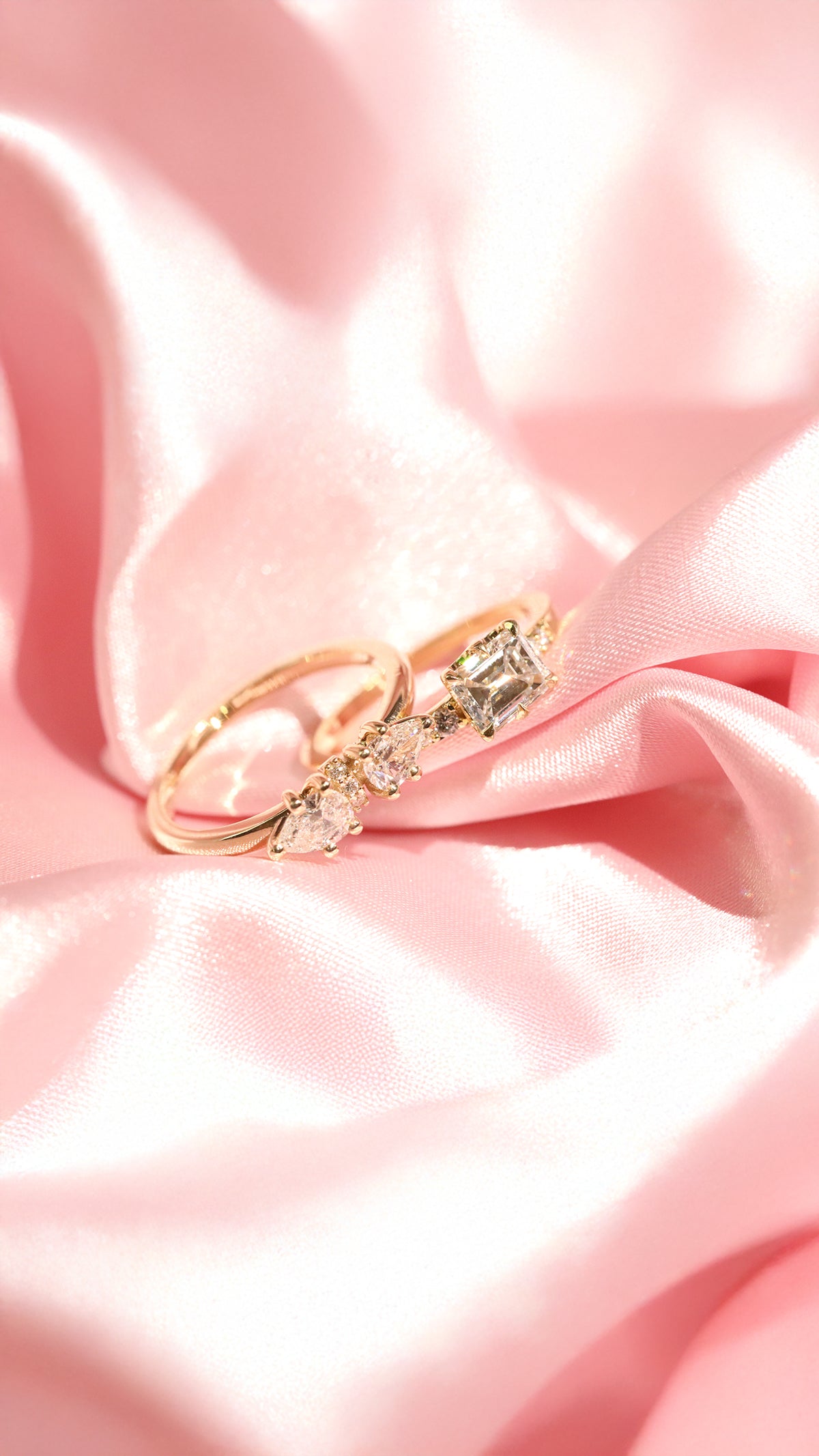 Two yellow gold engagement rings with white diamonds on a pink satin background