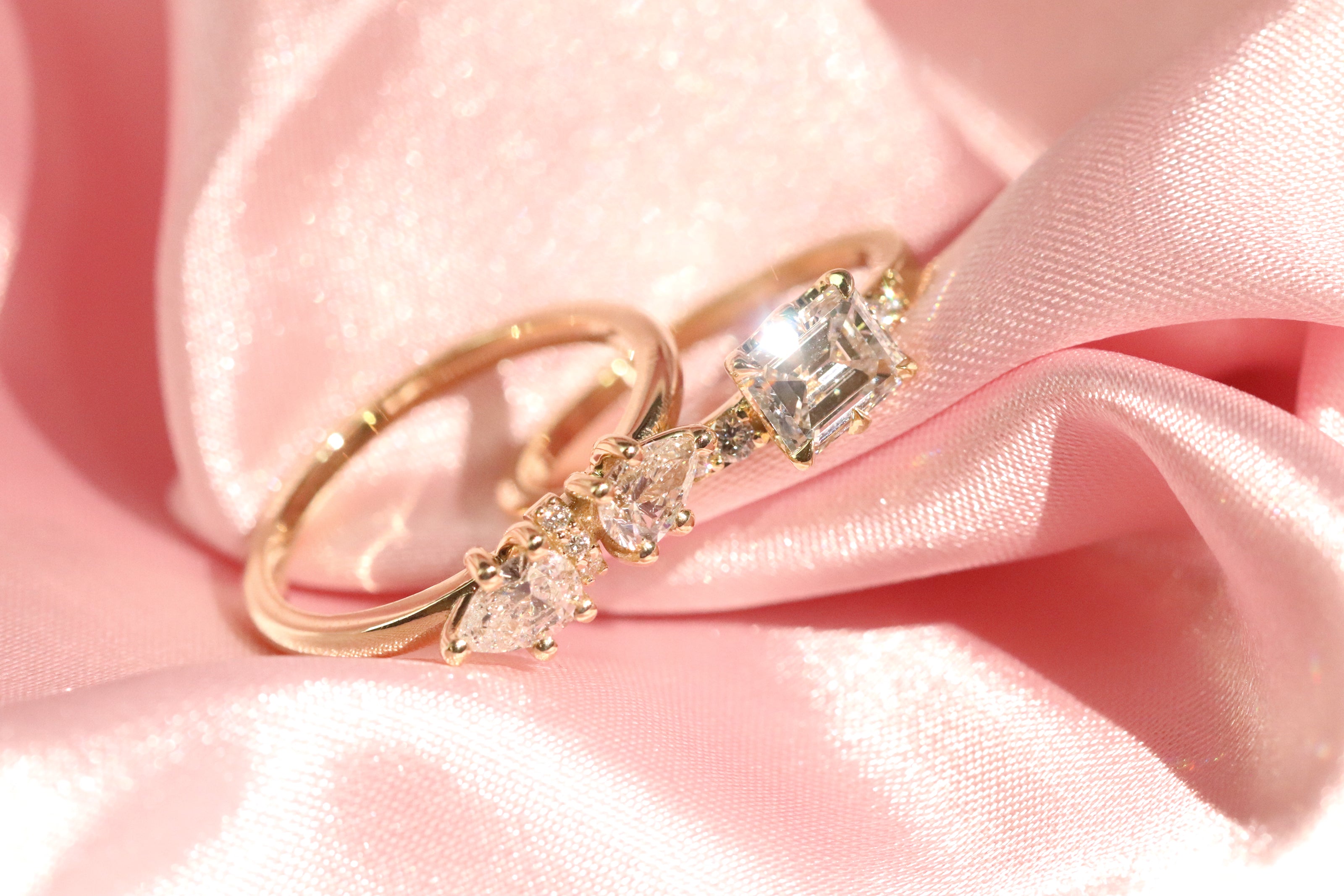 Two yellow gold engagement rings with white diamonds on a pink satin background