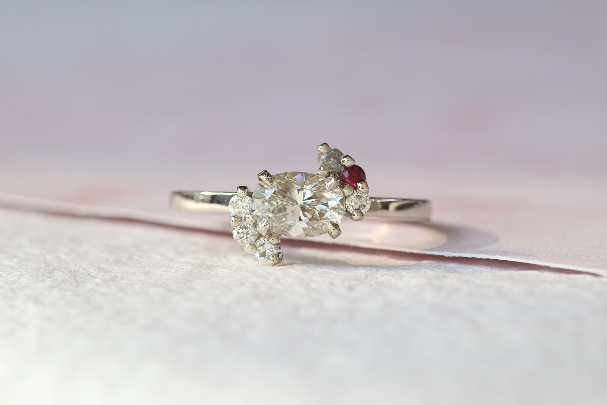 Custom engagement ring featuring a center white diamond and cluster of white diamonds, salt and pepper diamonds, and a red ruby on the platinum band.